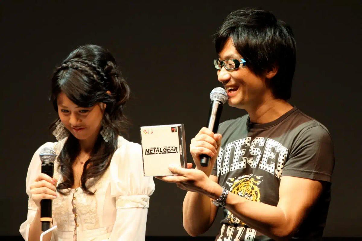 Hideo Kojima segurando uma caixa do jogo Metal Gear enquanto fala ao microfone.